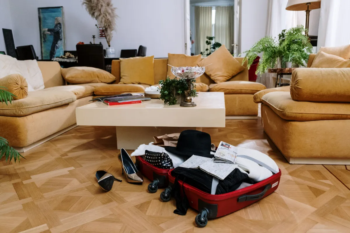 An open suitcase on a living-room floor surrounded by folded clothes and storage boxes